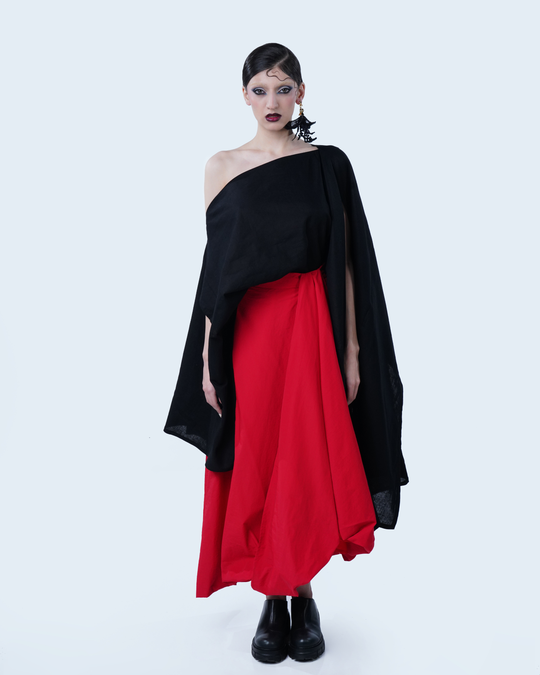 Model wearing Hüna Draped Skirt – red mid-length skirt in lightweight polyester with asymmetrical drape and sculptural volume from the Volume Noir Collection.